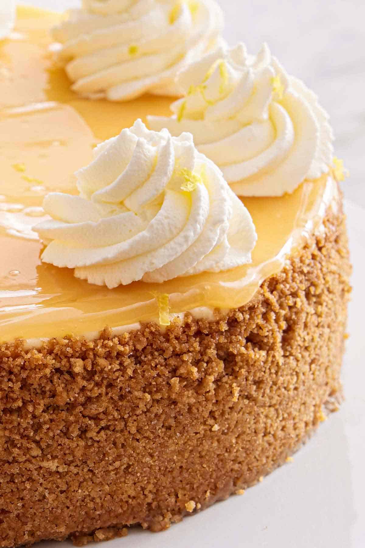 Close up of a graham cracker crust from a cheesecake with dollops of whipped cream on top.