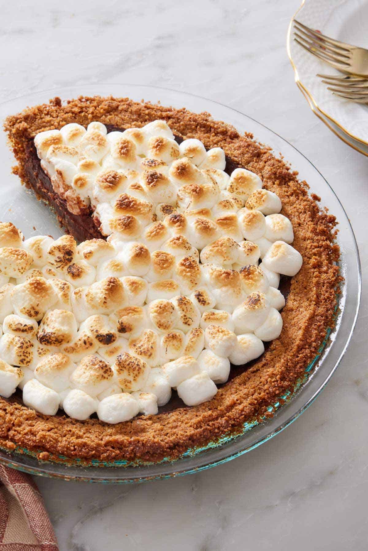 A pie with toasted marshmallows in a graham cracker crust with a slice cut out.