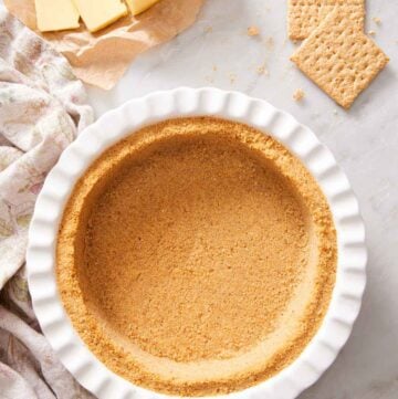 Overhead view of a pie dish containing a graham cracker crust. Butter and graham crackers in the background.