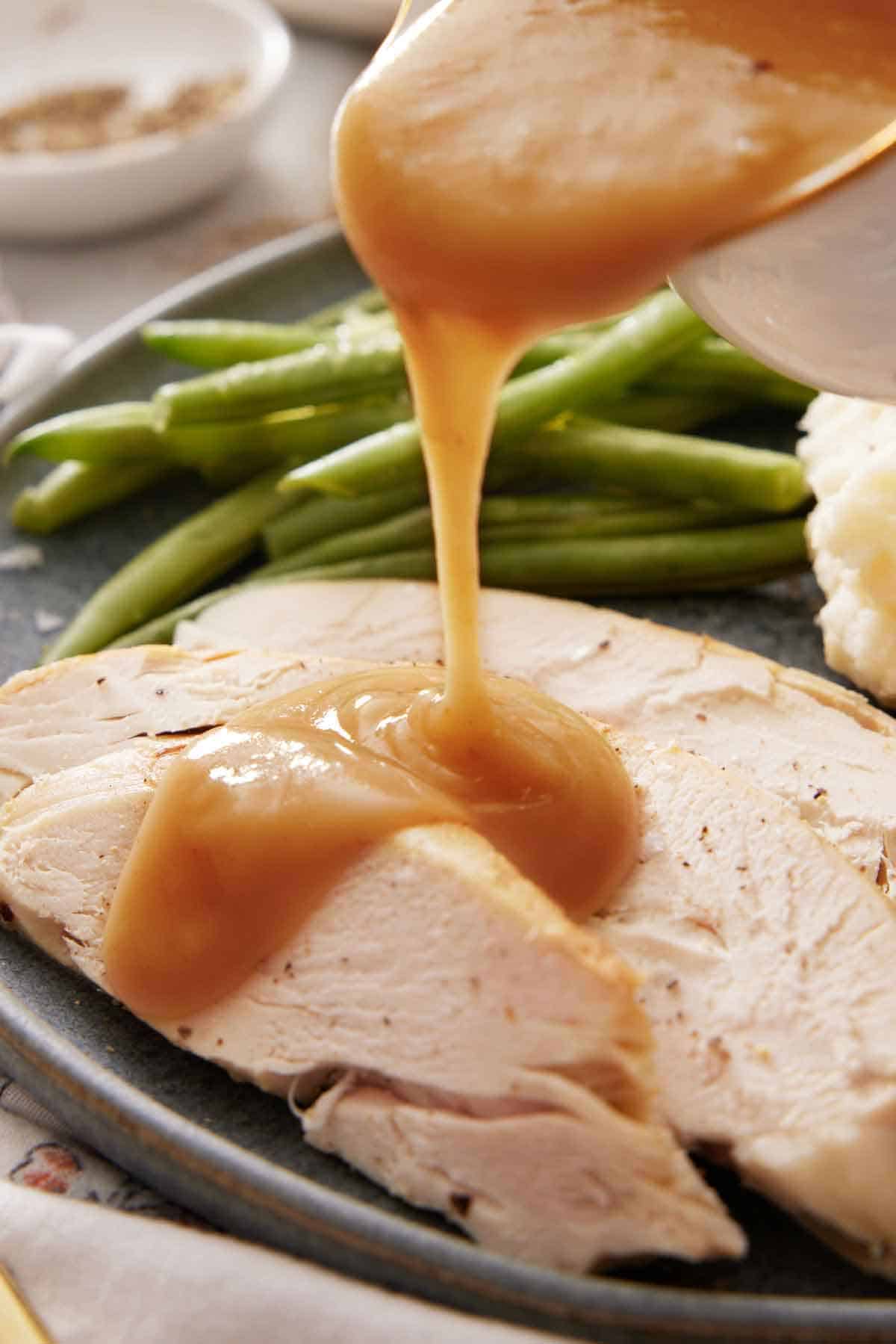 Gravy poured over sliced turkey meat on a plate with green beans.