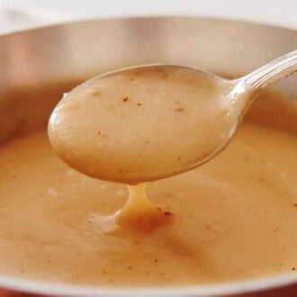 Gravy in a spoon lifted from a pot.