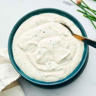 Overhead view of a bowl of horseradish sauce with a spoon. Chives and a napkin on the side.