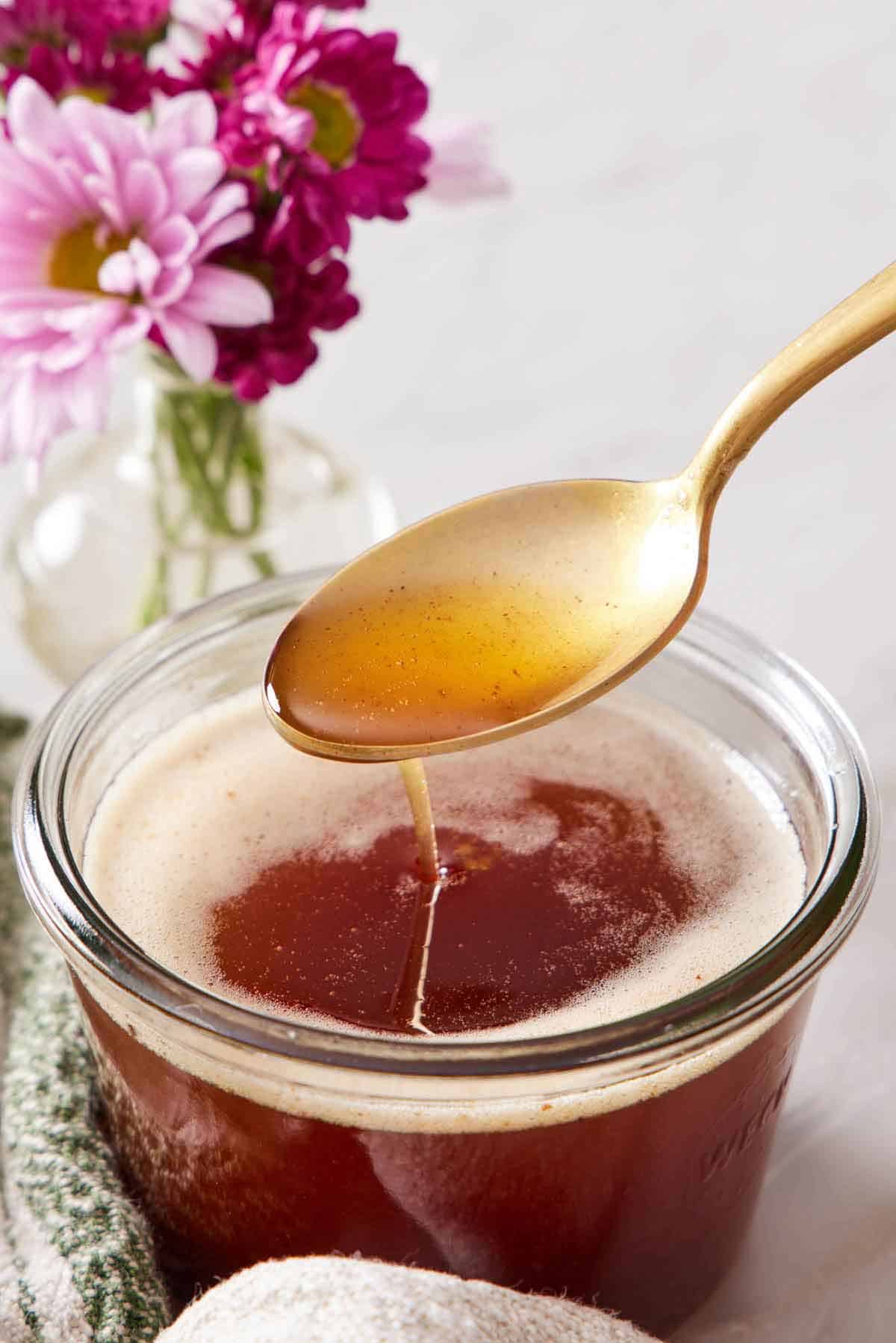 A spoonful of brown butter lifted from a jar. Pink flowers in the background.