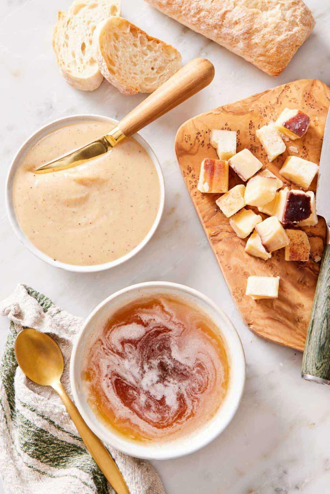 Overhead view of a bowl of brown butter and whipped butter. A spoon, bread, and a knife with a board on the side.