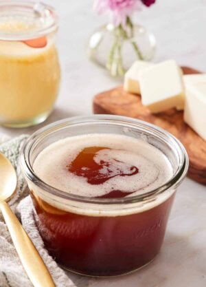 A jar of brown butter. A spoon beside it and a stick of cut butter in the background.
