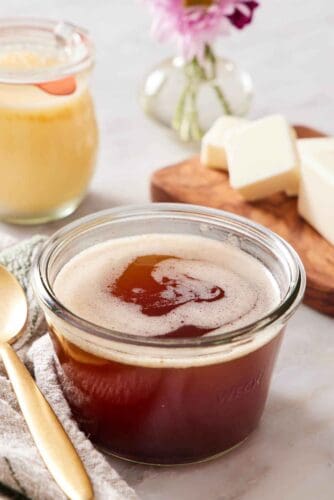 A jar of brown butter. A spoon beside it and a stick of cut butter in the background.