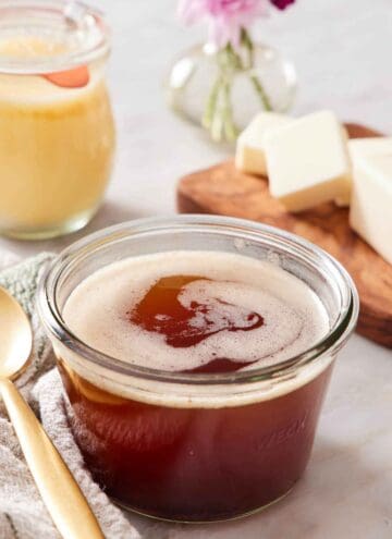 A jar of brown butter. A spoon beside it and a stick of cut butter in the background.