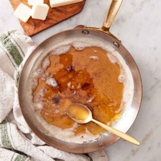 Overhead view of a skillet of brown butter with a spoon inside on a linen napkin.