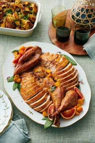 A platter with a carved turkey. Drinks in the background along with stuffing.