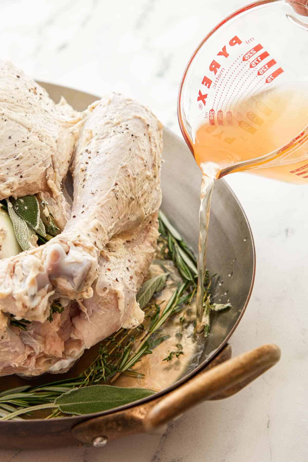 Broth poured into the baking dish with herbs and a turkey.