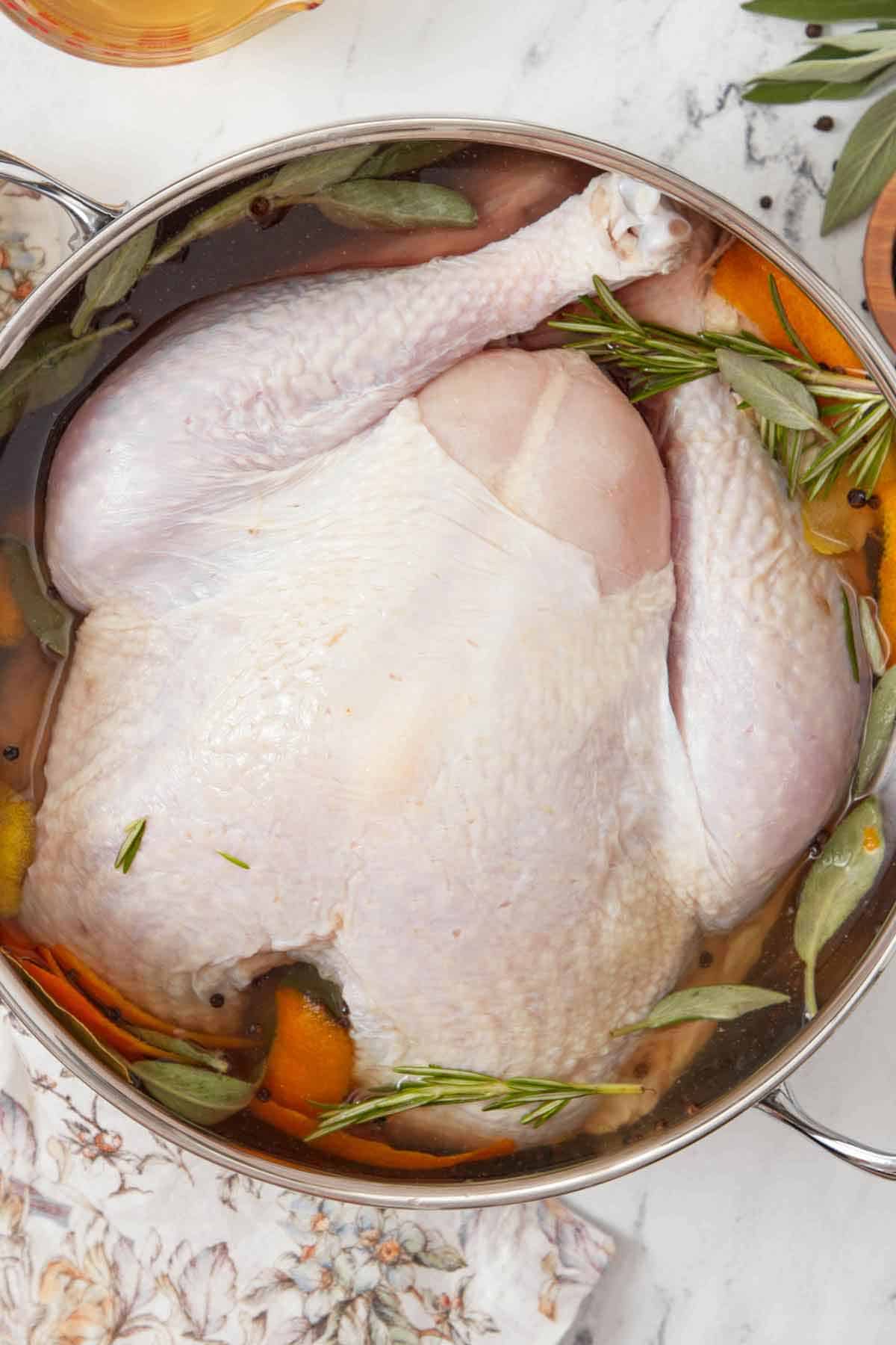 Overhead view of a turkey in a pot of liquid and aromatics.