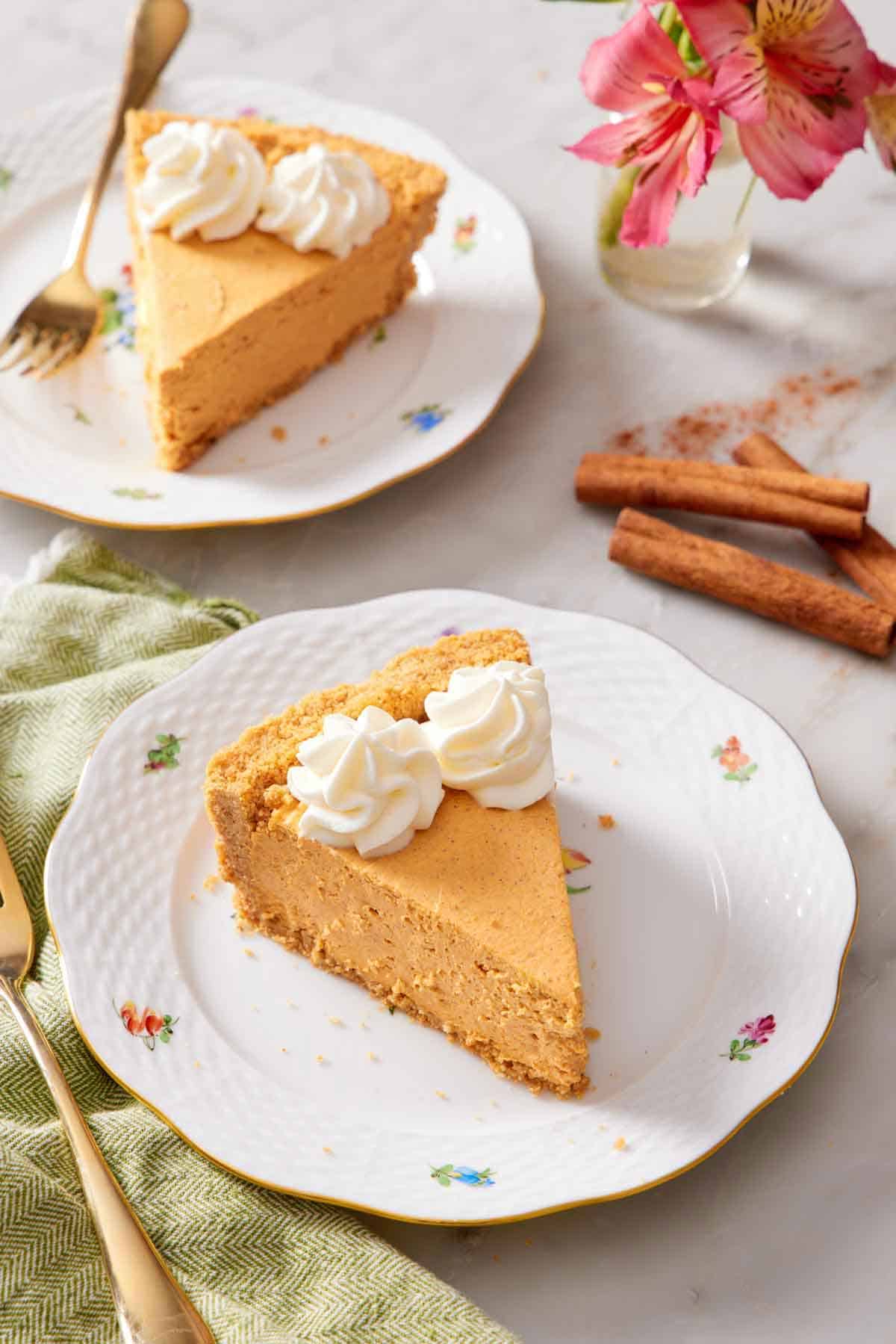 Two plates with sliced no-bake pumpkin cheesecake. Cinnamon sticks, flowers, and forks on the side.