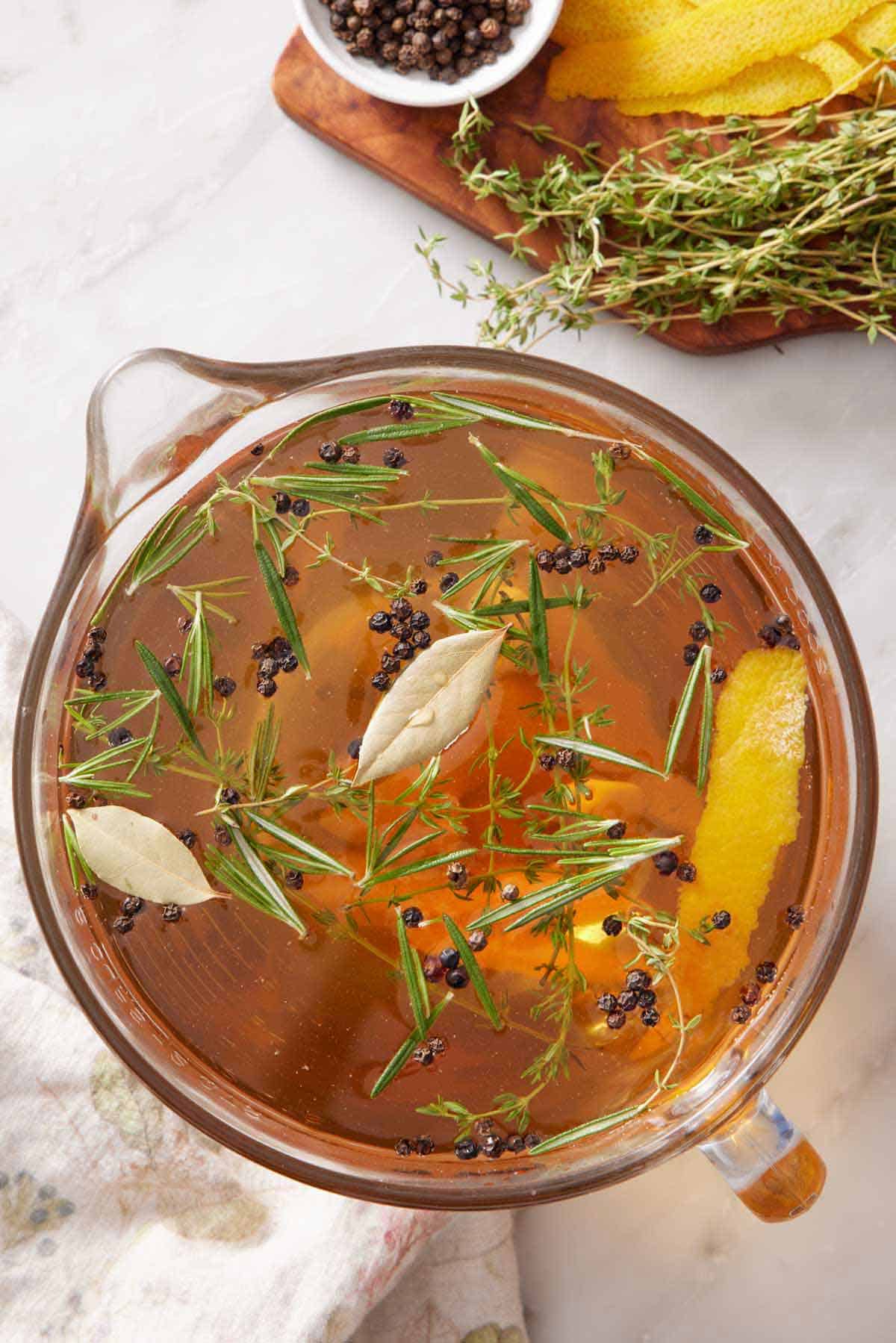 Overhead view of a large measuring cup of turkey brine with more loose ingredients off to the side.