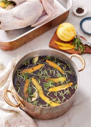 A pot of turkey brine with more ingredients in the background along with a raw turkey.