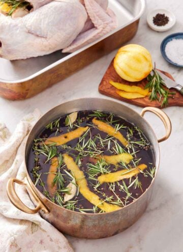 A pot of turkey brine with more ingredients in the background along with a raw turkey.