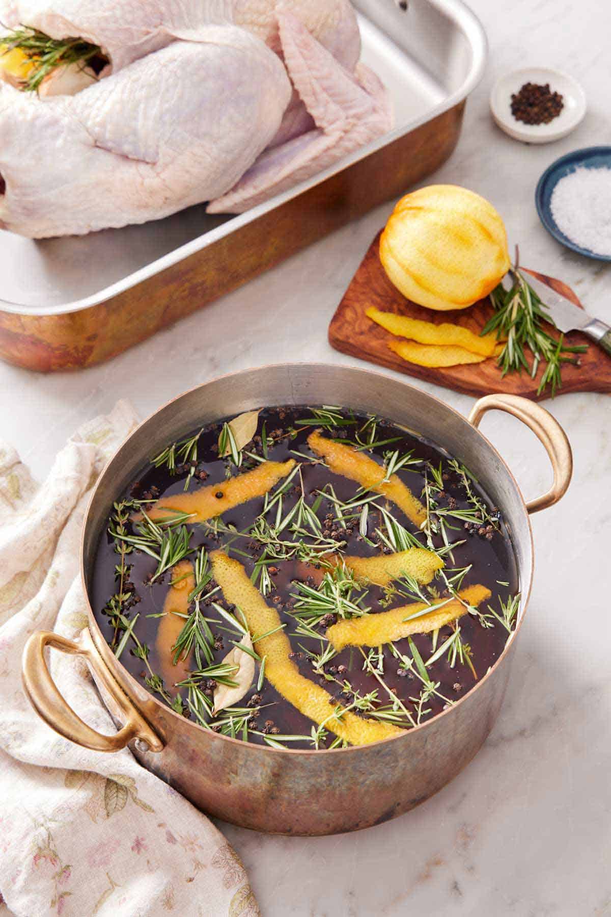 A pot of turkey brine with more ingredients in the background along with a raw turkey.