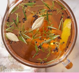 Pinterest graphic of a large measuring cup of turkey brine with more herbs off to the side.