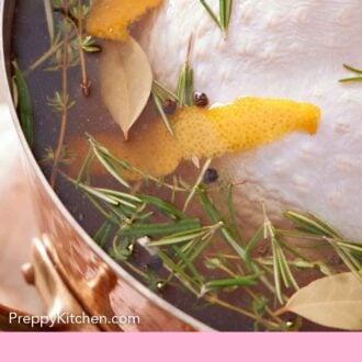 Pinterest graphic of a close up view of a submerged turkey in a brine with herbs, peppercorn, and orange zest.