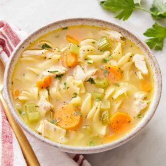 A bowl of turkey noodle soup with parsley off to the side along with a linen napkin and spoon.