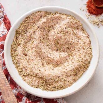 Overhead view of a bowl of turkey seasoning with a spoon on the side and some paprika and dried herbs.