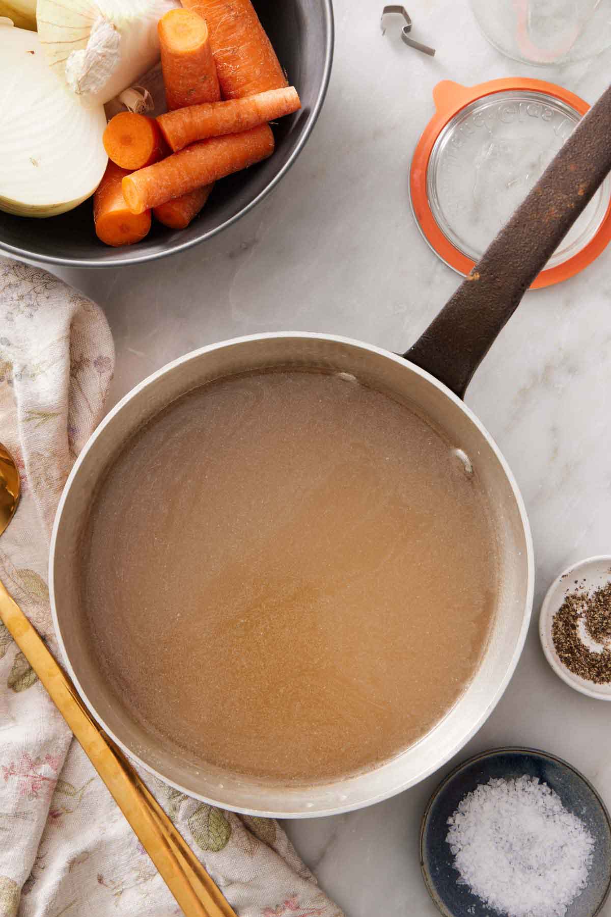 An overhead view of a pot of turkey stock. A bowl of salt, pepper, and aromatics.