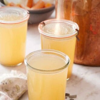 Pinterest graphic of three jars of turkey stock, the one in the front with the lid off. Stock pot in the background along with some aromatics.