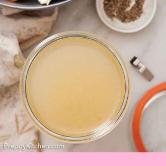 Pinterest graphic of an overhead of a jar of turkey stock. Aromatics and a bowl of pepper off to the side.