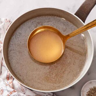 A ladle lifting from a pot of turkey stock. Salt and pepper on the side.