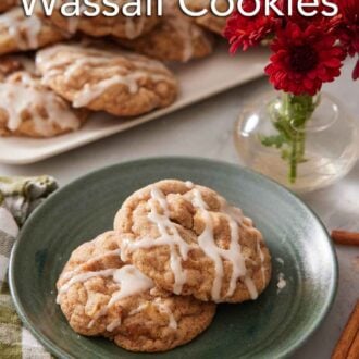 Pinterest graphic of a plate with two brown butter wassail cookies with a platter more in the background along with some red flowers.