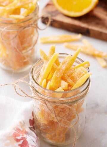 A mason jar full of candied orange peels with a twine bow on the jar. A second jar in the background.