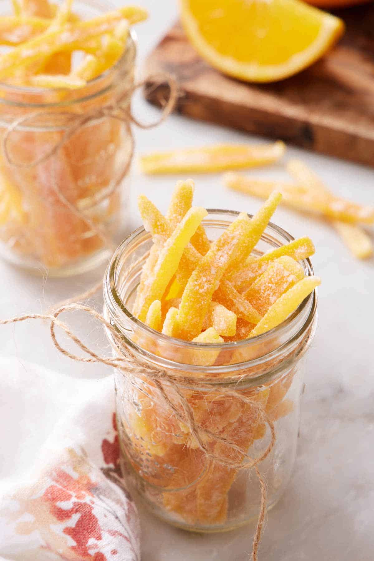 A mason jar full of candied orange peels with a twine bow on the jar. A second jar in the background.