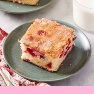 Pinterest graphic of A plate with a square slice of cranberry cake with another plated slice and glass of milk in the background.