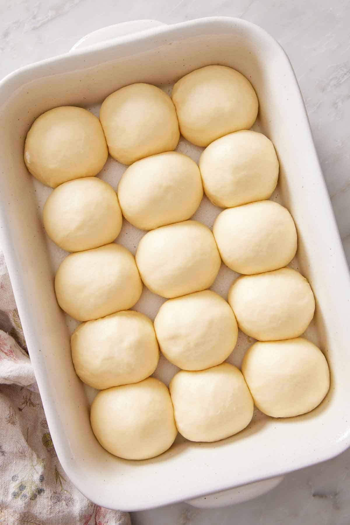 Overhead view of unbaked dinner rolls in a white baking dish.