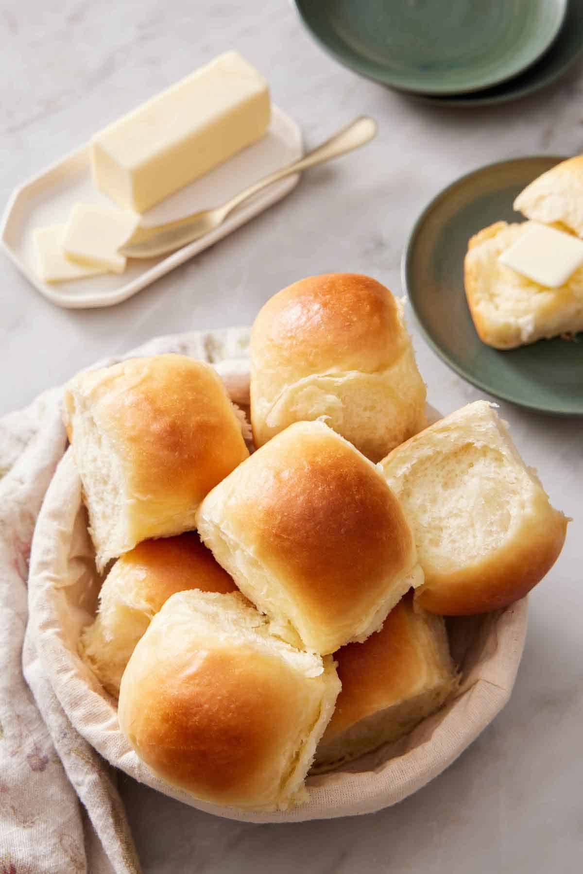 A basket of fluffy dinner rolls. Butter in the background.