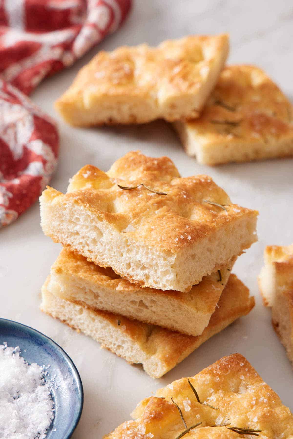 A stack of three pieces of focaccia with more scattered around on a marble surface.