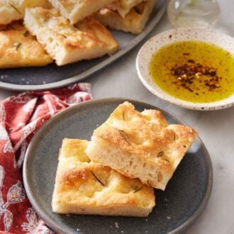 Pinterest graphic of a plate with two pieces of focaccia with more on a platter in the background along with a bowl of oil.