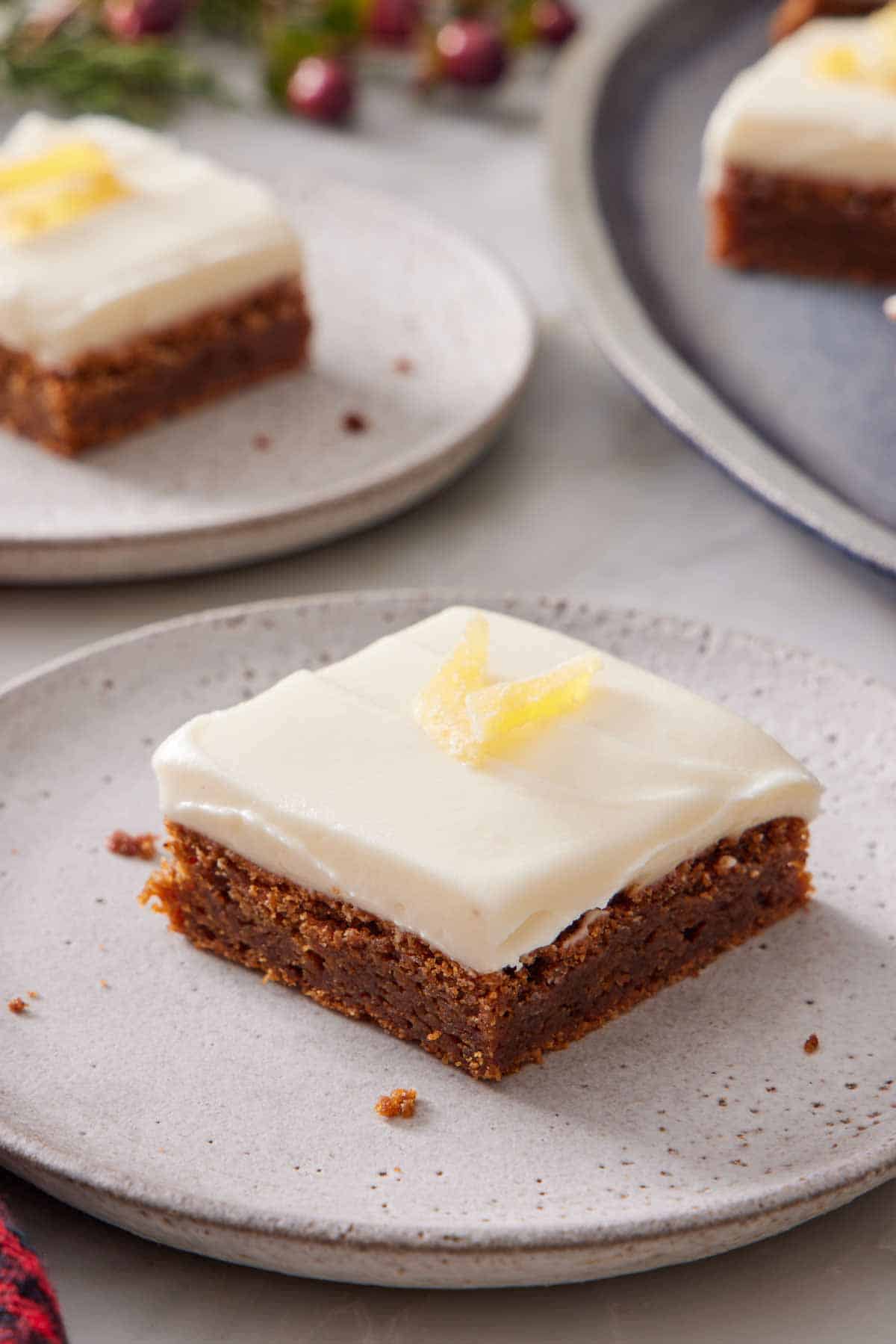 A slice of gingerbread bars topped with candied ginger with more plated slices in the background, out of focus.