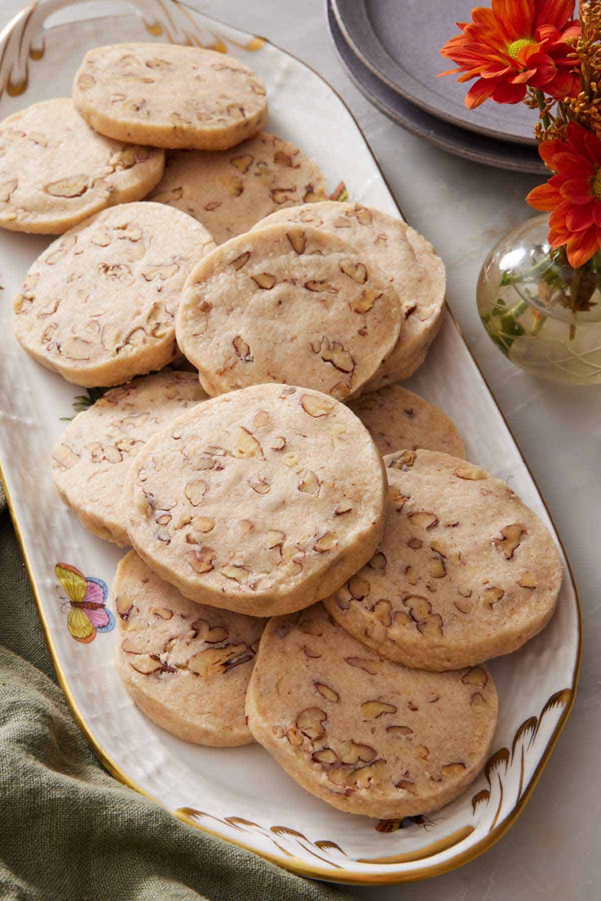 A platter of pecan shortbread cookies with a small vase of flowers on the side with plates and a napkin.