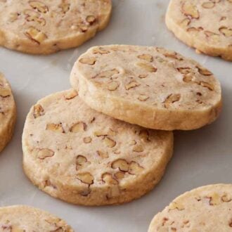 Multiple pecan shortbread cookies on a marble surface with one cookie in the middle leaning on another.