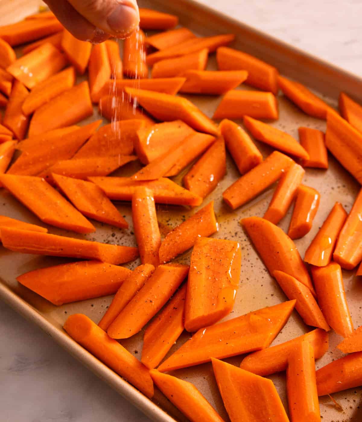 A pinch of salt sprinkled over carrots on a sheet pan.