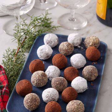 A blue platter of rum balls with various coatings. Glasses and a bottle of champagne in the background.