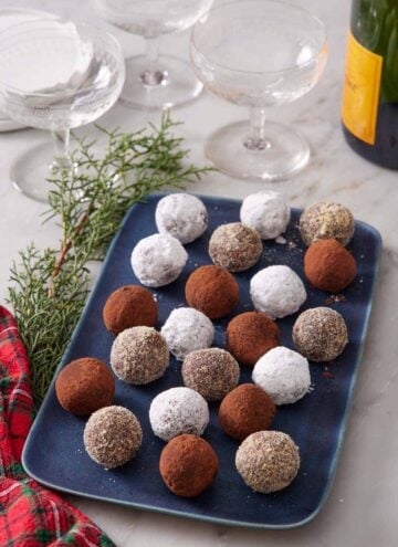 A blue platter of rum balls with various coatings. Glasses and a bottle of champagne in the background.