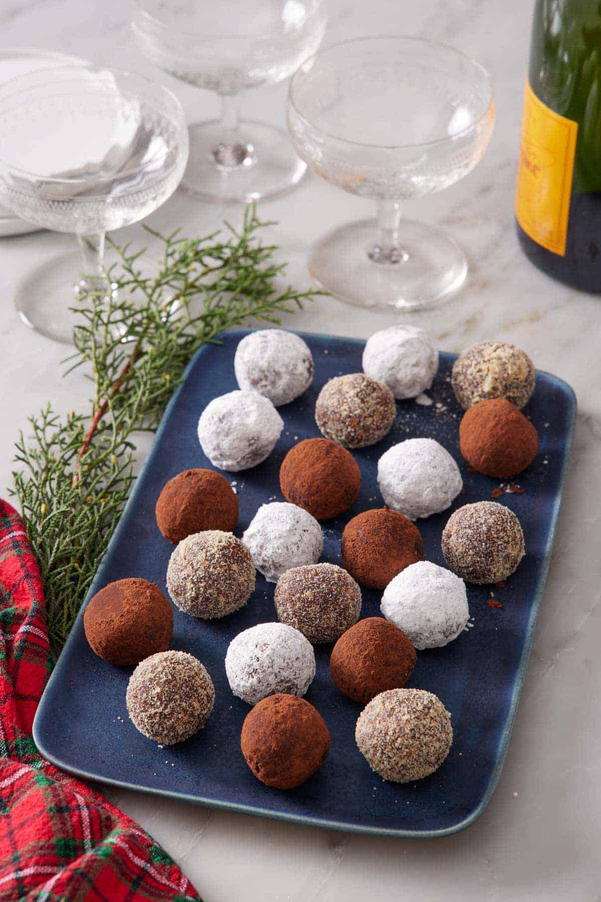 A blue platter of rum balls with various coatings. Glasses and a bottle of champagne in the background.