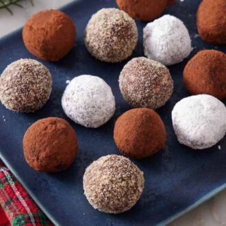 A blue platter with rum balls coated in various toppings. A holiday themed colored napkin on the side.