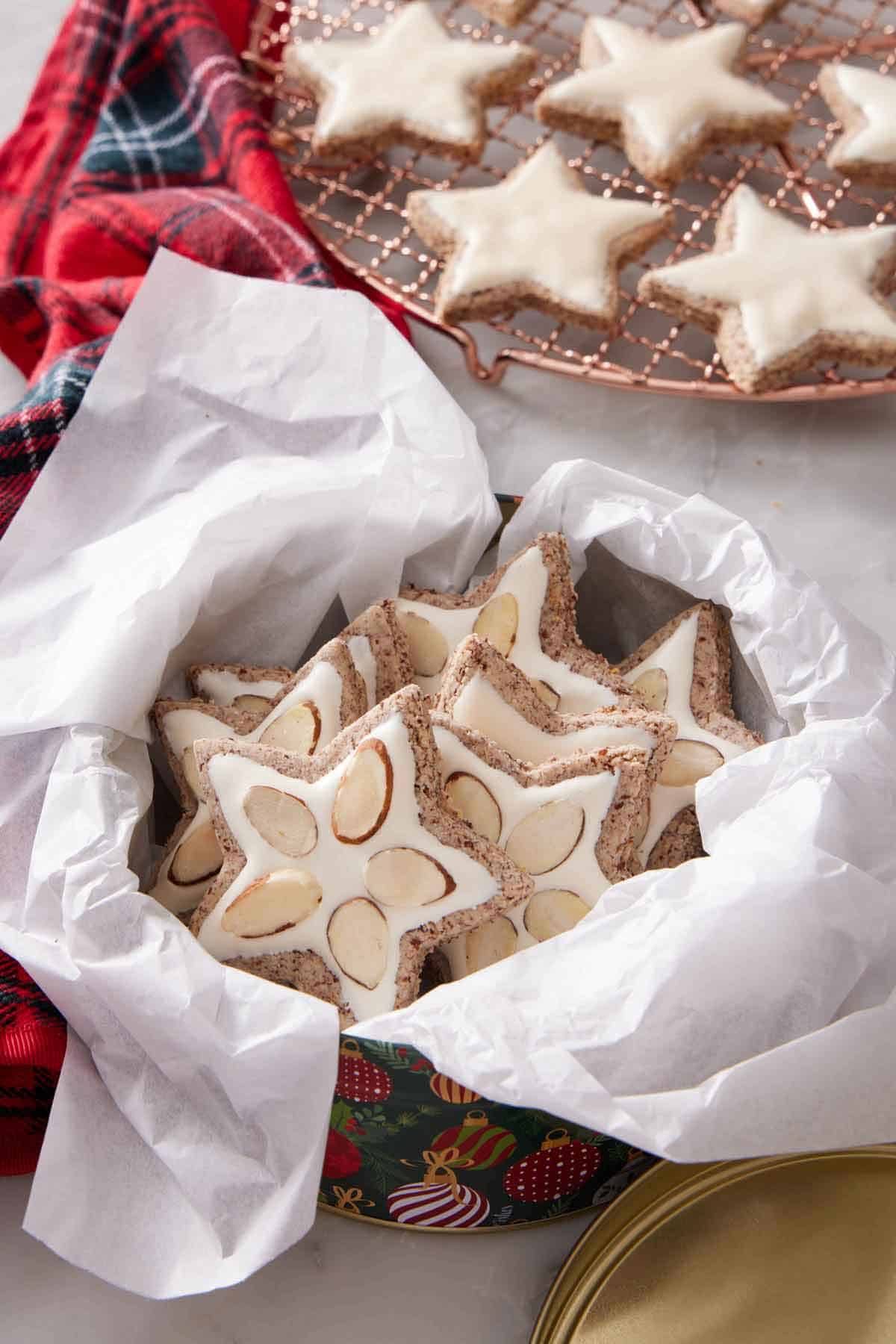 A round tin lined with parchment paper with zimtsterne with sliced almonds.