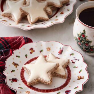 Pinterest graphic of a plate with two star shaped zimtsterne with more in the background on a larger platter.