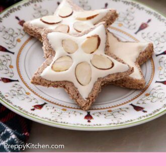 Pinterest graphic of a plate with three star shaped zimtsterne with two with sliced almonds in the icing.