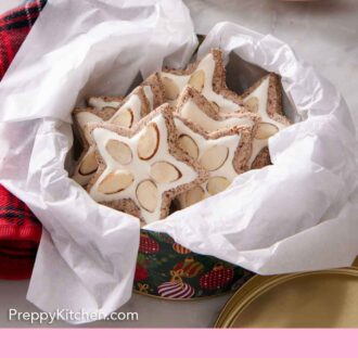 Pinterest graphic of a tin lined with parchment paper with zimtsterne with sliced almonds.