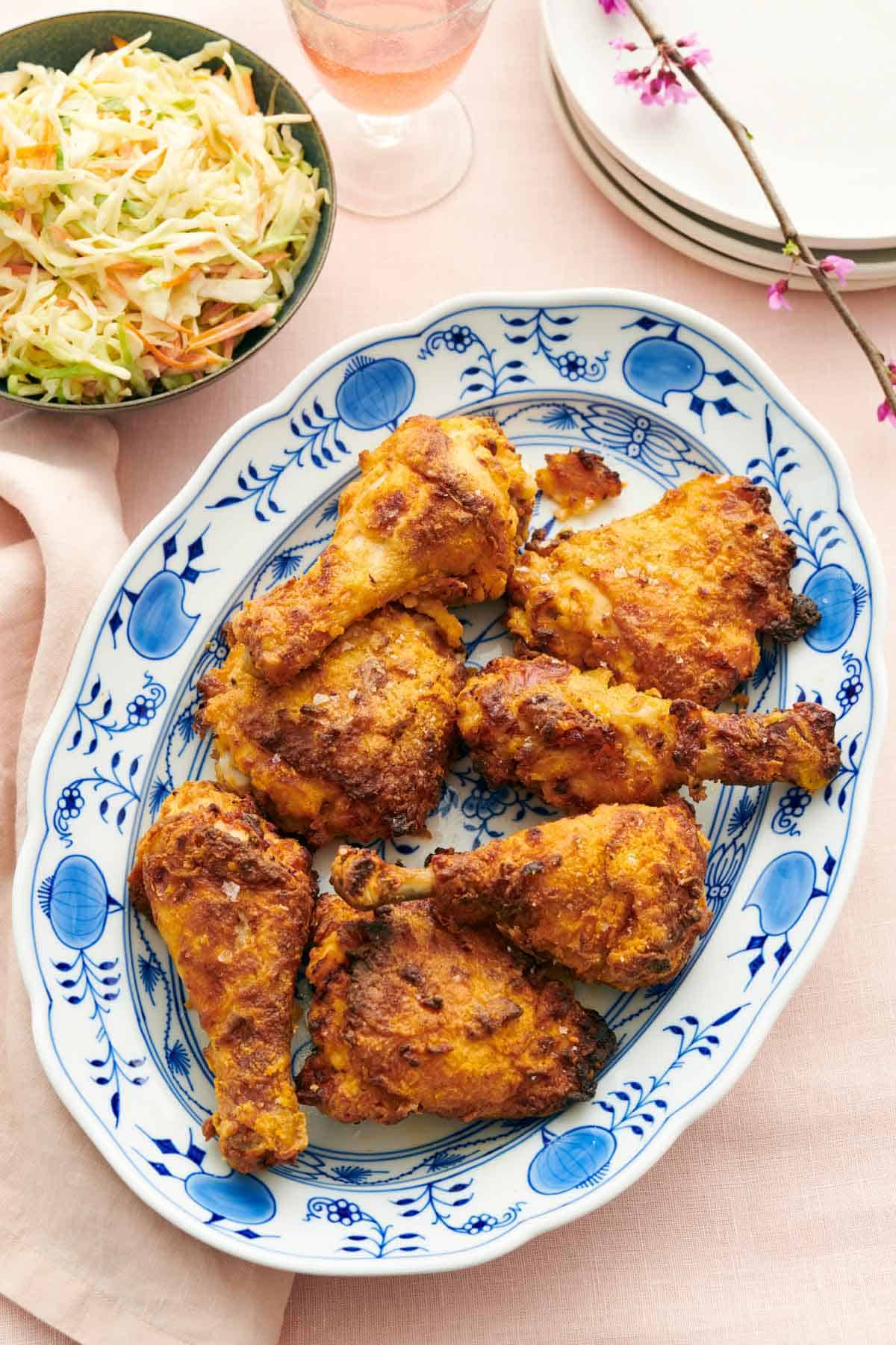 Overhead view of a platter of air fryer fried chicken with a bowl of coleslaw on the side along with a stack of plates.