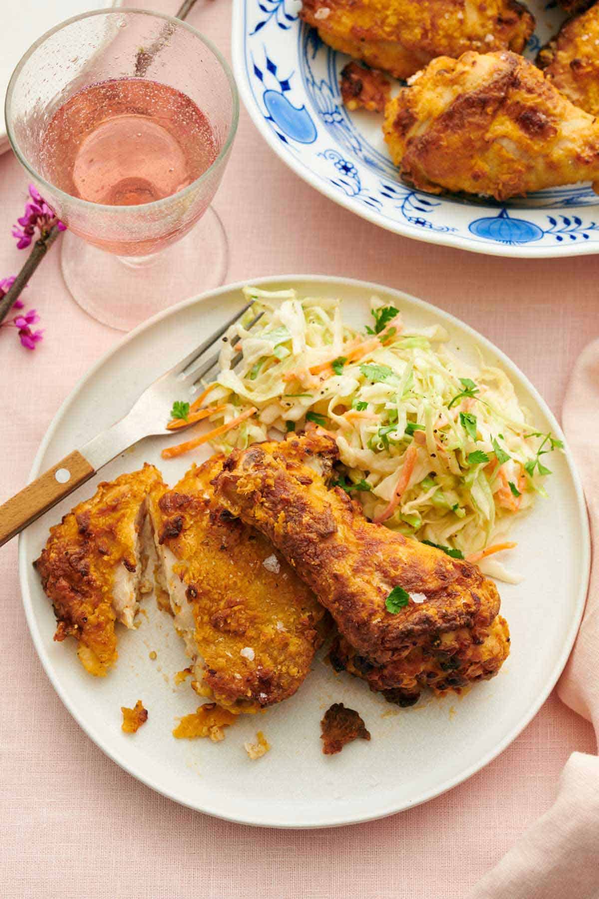 Overhead view of two pieces of air fryer fried chicken on a plate with coleslaw and fork. A bubbly drink and more chicken on the side.